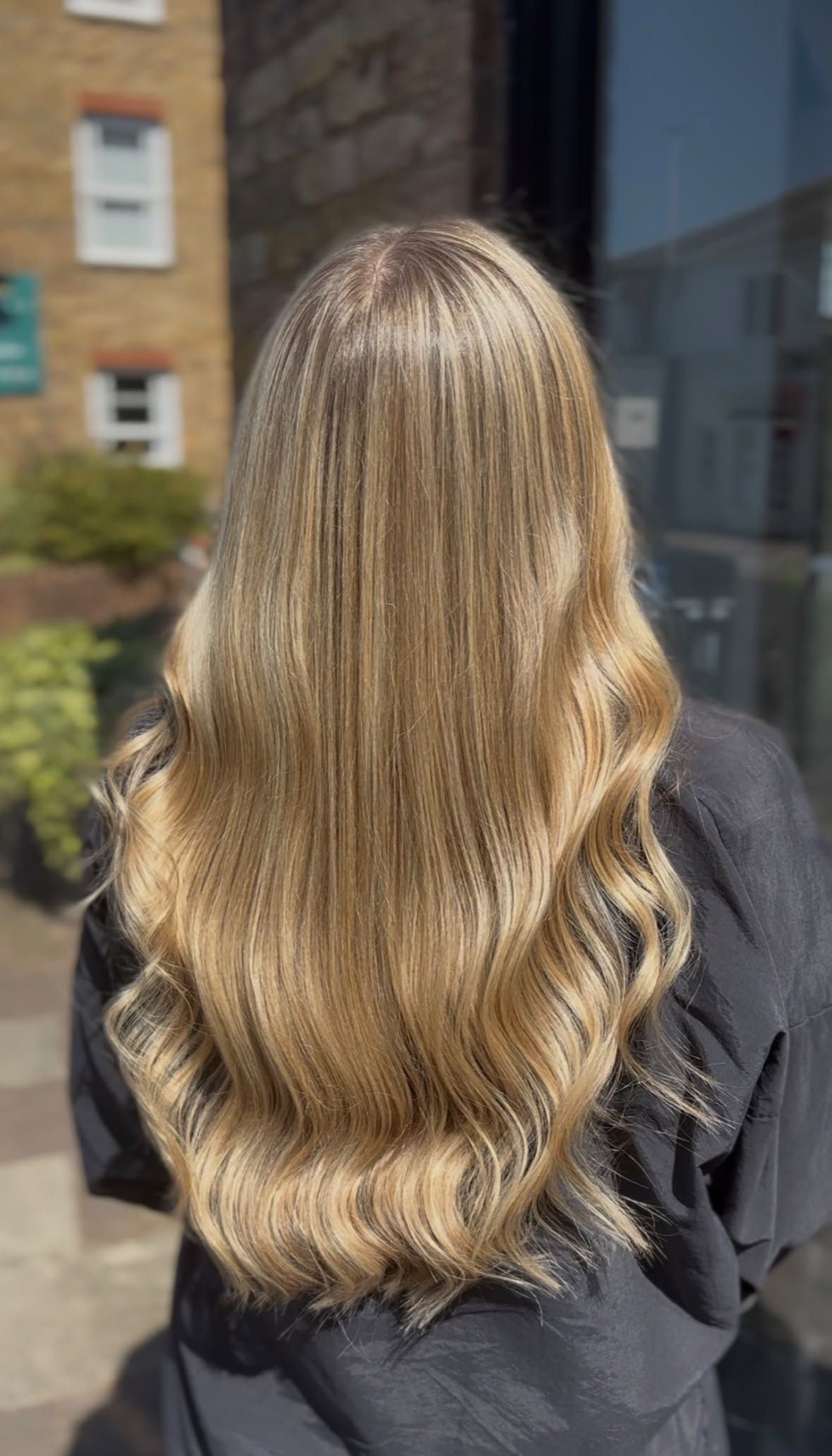 Long golden balayage finished with soft waves, photographed outside on a London street