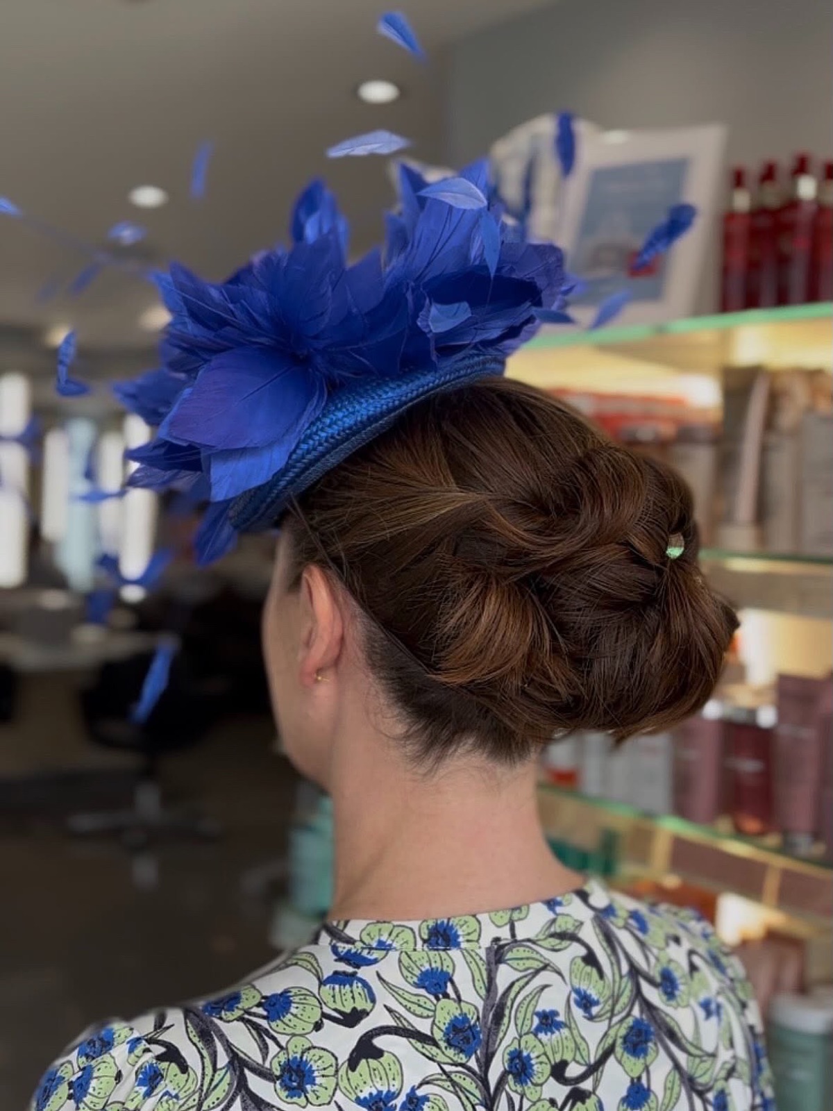 Sculpted brunette chignon finished with a blue feather fascinator